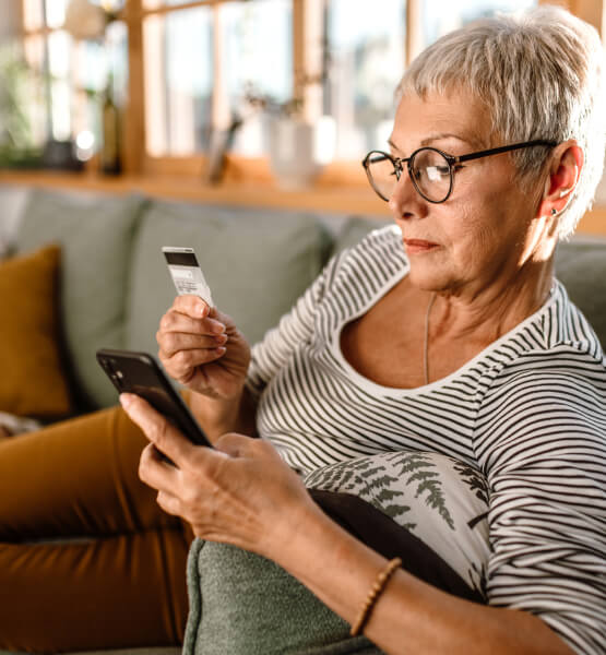 Mature woman relaxing on her couch while holding her debit card and smart phone