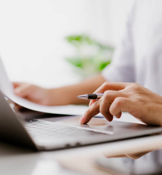 person typing on laptop holding pen
