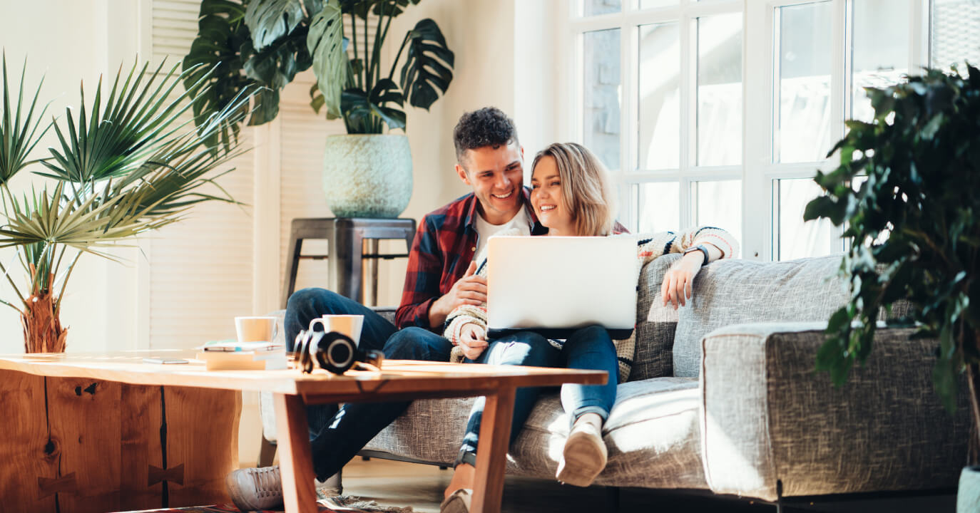 A couple sitting on their couch looking at a laptop together